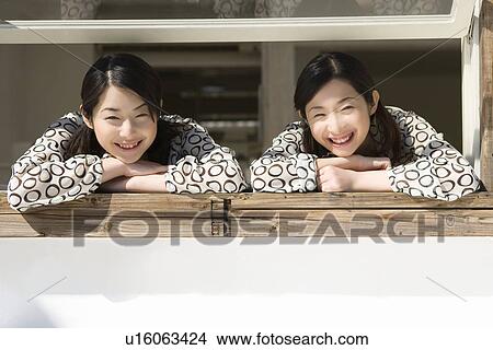 Portrait of twin sisters at the window, smiling and looking at camera, front view View Large Photo Image Picture - Portrait of twin sisters at the window, smiling and looking at camera, front view. Fotosearch