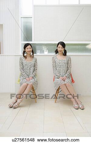 Portrait of twin sisters sitting on chairs, smiling and looking at camera, front view View Large Photo Image Stock Photo - Portrait of twin sisters sitting on chairs, smiling and looking at camera, front view. Fotosearch