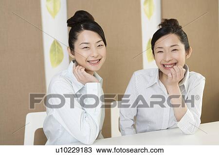 Stock Image - Portrait of twin sisters, smiling and looking at camera, front view. Fotosearch