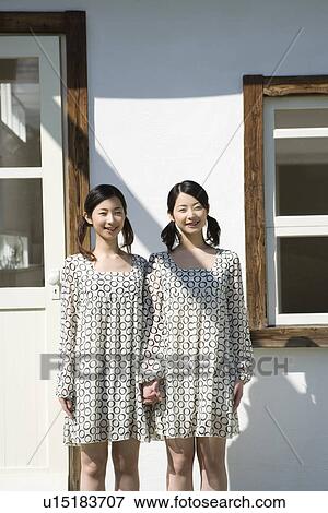 Portrait of twin sisters standing together beside the window, smiling and looking at camera, front view View Large Photo Image Stock Photo - Portrait of twin sisters standing together beside the window, smiling and looking at camera, front view. Fotosearch