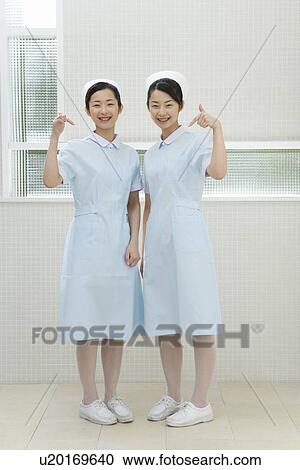 Stock Image - Portrait of two nurses, twin sisters, smiling and looking at camera, front view. Fotosearch