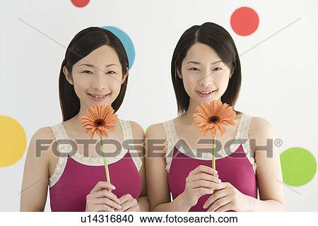 Portrait of Two Young Twin Sisters Holding Flowers of Gerbera, Smiling, Front View View Large Photo Image Stock Image - Portrait of Two Young Twin Sisters Holding Flowers of Gerbera, Smiling, Front View. Fotosearch