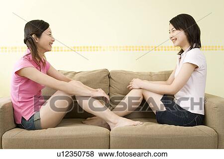 Stock Photo - Portrait of Two Young Twin Sisters Sitting on Sofa, Face to Face, Smiling, Side View. Fotosearch