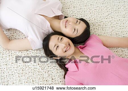 Stock Photo - Portrait of Two Young Twin Sisters Lying on Back, Smiling, High Angle View. Fotosearch
