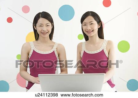 Stock Photo - Portrait of Two Young Twin Sisters Using a Laptop, Front View . Fotosearch
