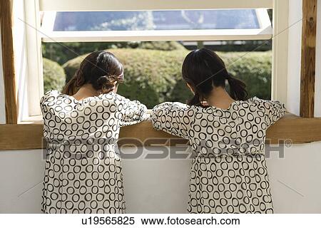 Stock Photography - Twin sisters looking outside the window, rear view. Fotosearch