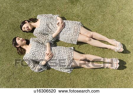 Stock Image - Twin sisters lying down on lawn, smiling, high angle view. Fotosearch