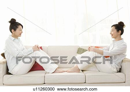 Twin sisters sitting on couch and smiling to each other, side view View Large Photo Image Stock Image - Twin sisters sitting on couch and smiling to each other, side view. Fotosearch