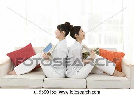 Twin sisters sitting on couch and holding books, back to back, smiling, side view View Large Photo Image Stock Photography - Twin sisters sitting on couch and holding books, back to back, smiling, side view. Fotosearch