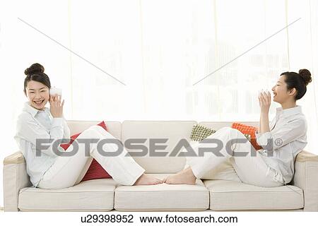 Twin sisters sitting on couch and using string telephones, smiling, side view View Large Photo Image Stock Image - Twin sisters sitting on couch and using string telephones, smiling, side view. Fotosearch