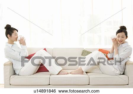 Twin sisters sitting on couch and using string telephones, smiling, side view View Large Photo Image Stock Photograph - Twin sisters sitting on couch and using string telephones, smiling, side view. Fotosearch