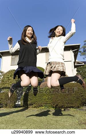 Stock Photo - Twin sisters smiling and jumping in garden, front view. Fotosearch