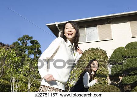 Stock Photo - Twin sisters smiling and running in garden, side view. Fotosearch