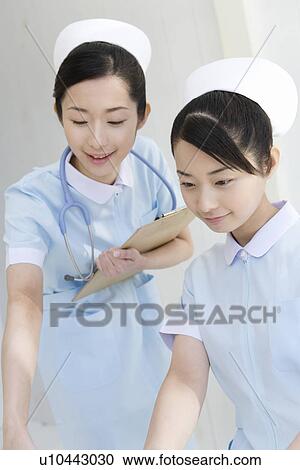 Stock Image - Two nurses working together, twin sisters, front view. Fotosearch