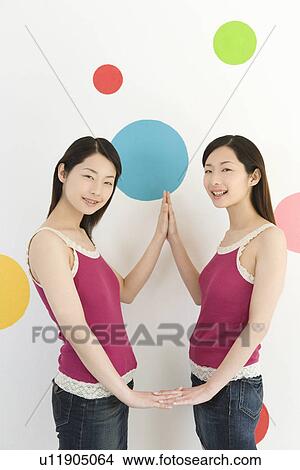 Picture - Two Young Twin Sisters Posing in front of Polka Dots of Wall Paper, Side View. Fotosearch