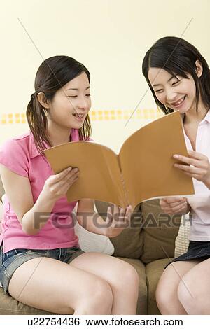 Stock Photograph - Two Young Twin Sisters Reading a Book, Smiling, Front View. Fotosearch