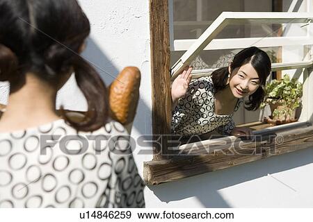 Stock Photo - Woman looking her sister holding a shopping bag from the window, side view, rear view. Fotosearch
