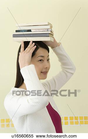 Stock Photography - Young Woman Balancing Books on Her Head, Smiling, Side View. Fotosearch