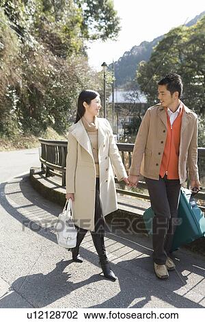 Stock Image - Japanese couple walking hand in hand, front view, Japan. Fotosearch