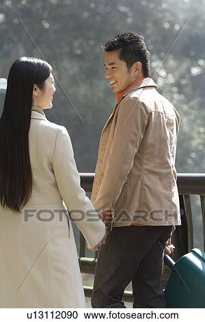 Stock Image - Japanese couple walking hand in hand, rear view, side view, Japan. Fotosearch
