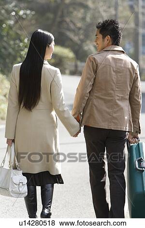Stock Photo - Japanese couple walking hand in hand, rear view, Japan. Fotosearch