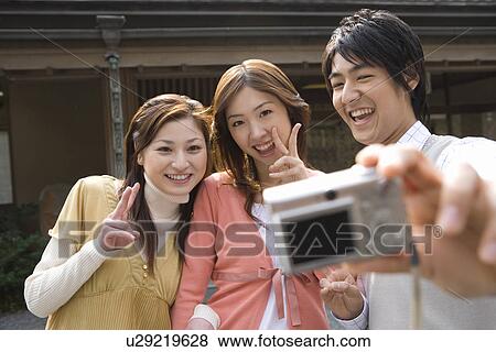 Stock Photo - Three young people taking a picture of themselves, front view, Japan. Fotosearch