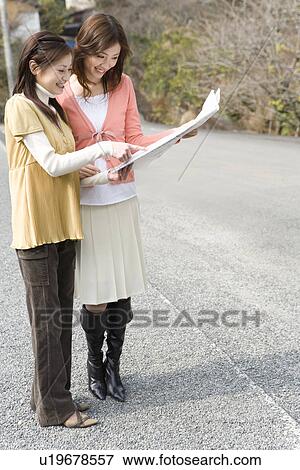 Stock Photo - Two women looking at a map on the road, side view, Japan. Fotosearch