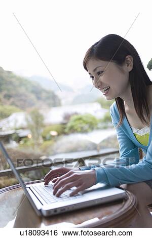 Stock Photograph - Woman smiling and using laptop, side view, Japan. Fotosearch