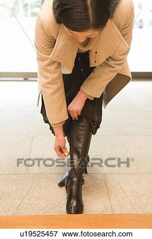 Stock Photo - Woman taking a boot off at the entrance of the Japanese inn, front view, Japan. Fotosearch