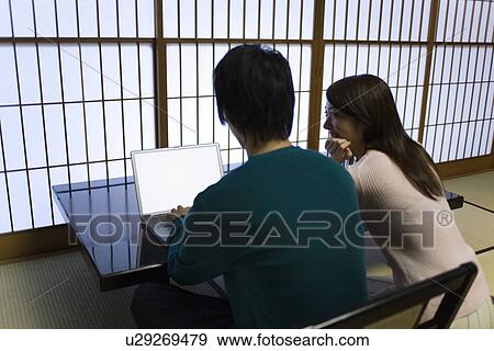 Stock Photo - Young couple using laptop, rear view, side view, Japan. Fotosearch