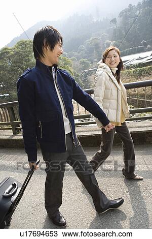 Stock Image - Young couple walking hand in hand, smiling, side view, Japan. Fotosearch