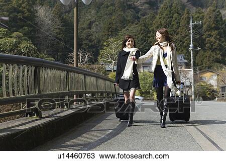 Young women walking hand in hand, carrying suitcases, front view, Japan View Large Photo Image Stock Image - Young women walking hand in hand, carrying suitcases, front view, Japan. Fotosearch