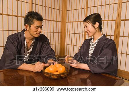 Stock Photo - Japanese couple in Yukata sitting in the room, woman holding an orange, front view, side view, Japan. Fotosearch