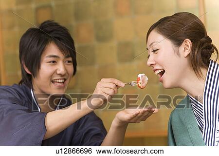 Stock Photograph - Man feeding woman a strawberry, smiling, front view, side view, Japan. Fotosearch