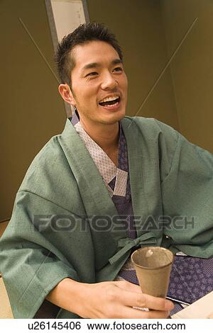 Stock Photograph - Man in Yukata smiling and holding a beer stein, front view, Japan. Fotosearch