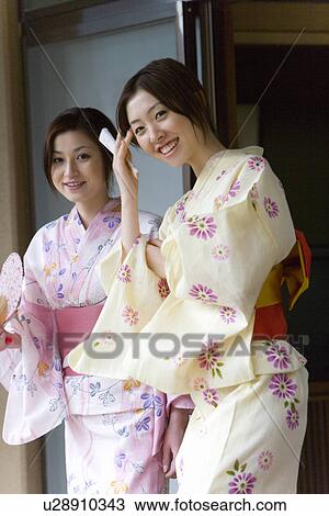 Stock Image - Portrait of two women in Yukata holding Japanese fans, smiling and looking at camera, front view, side view, Japan. Fotosearch
