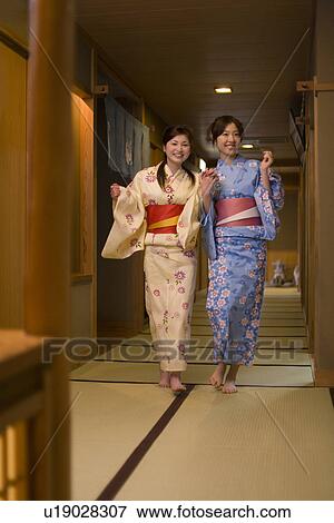 Stock Photo - Portrait of two women in Yukata walking hand in hand, front view, Japan. Fotosearch