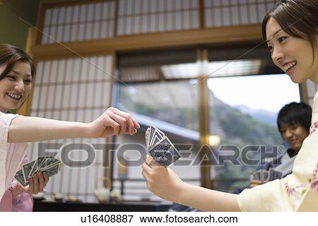 Stock Photo - Three young people in Yukata playing cards in Japanese inn, front view, side view, Japan. Fotosearch