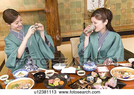 Stock Image - Two women having dinner, one taking a picture, front view, Japan. Fotosearch