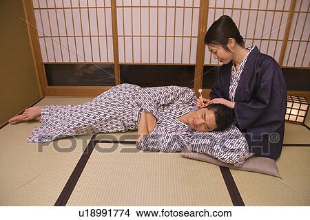 Picture - Woman cleaning man's ear in the room, front view, side view, Japan. Fotosearch