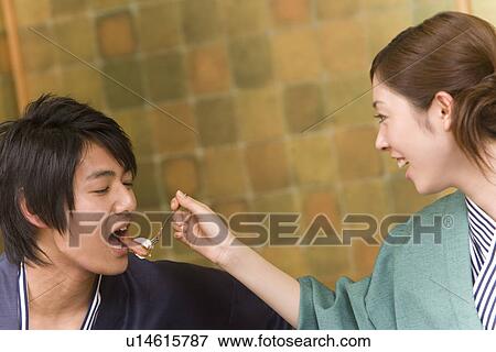 Stock Photo - Woman feeding man a strawberry, smiling, front view, side view, Japan. Fotosearch
