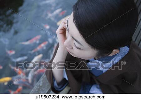 Picture - Woman in Yukata looking at the carps in pond, high angle view, close up, Japan. Fotosearch