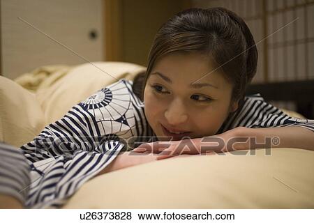 Stock Photo - Woman in Yukata smiling in bed, front view, Japan. Fotosearch