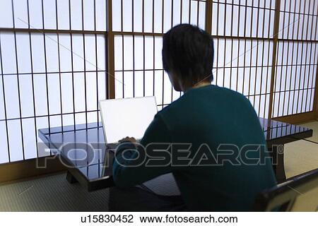 Stock Image - Young man using laptop, rear view, Japan. Fotosearch