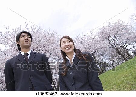 Stock Photo - Businessman and Businessman Standing in the Field with Cherry Trees, Waist Up, Low Angle View. Fotosearch