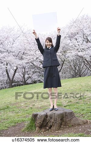 Stock Photography - Businesswoman Standing On A Tree Stump With Holding a White Board Up, Full Length, Front View. Fotosearch