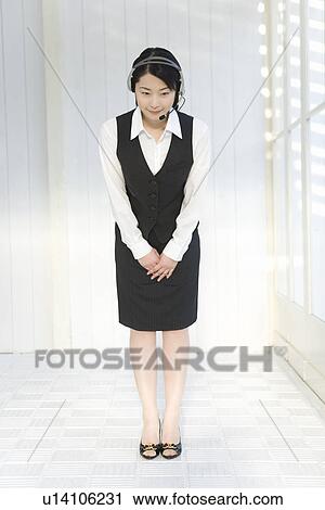 Stock Image - Portrait of a woman wearing hands-free headset, bending over, front view. Fotosearch