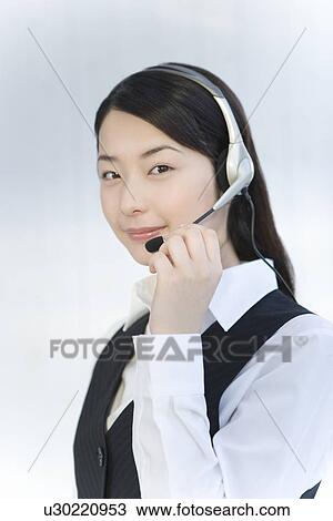 Stock Image - Portrait of a woman wearing hands-free headset, looking at camera, side view, white background. Fotosearch