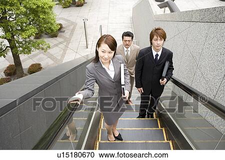 Stock Image - Three business people ascending escalator. Fotosearch