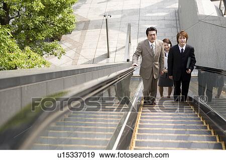 Three business people ascending escalator View Large Photo Image Stock Photo - Three business people ascending escalator. Fotosearch
